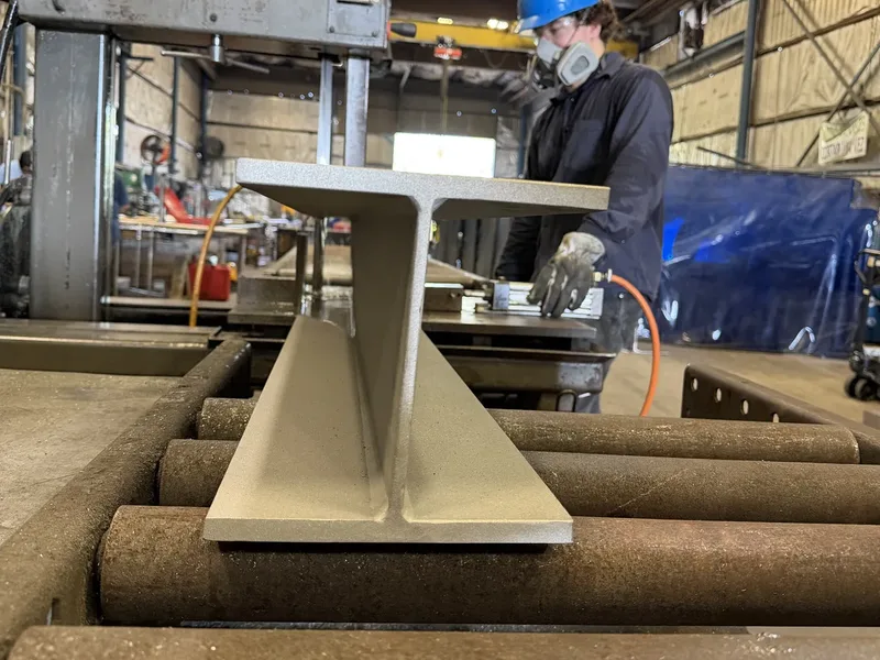 Stainless built-up beam on the roller table next to the band saw, a shop worker behind it